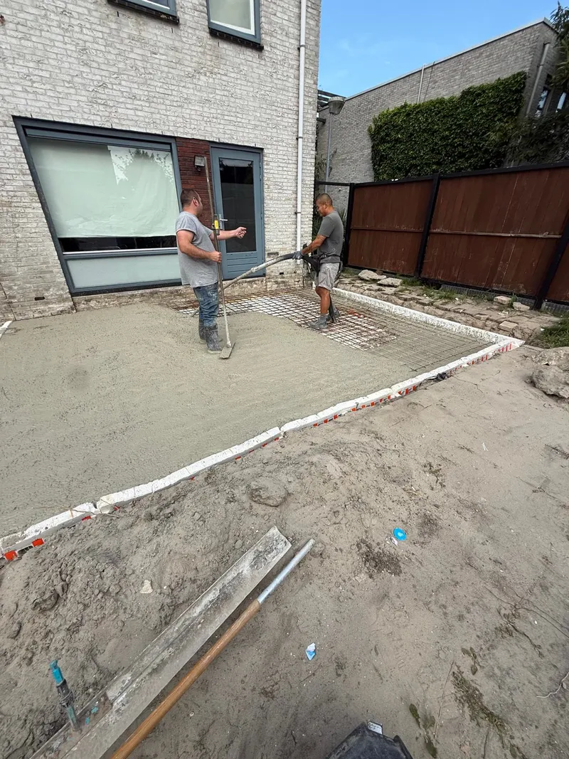 Twee vakmensen storten en verdelen het beton voor de vloer van een aanbouw achter een rijtjeshuis