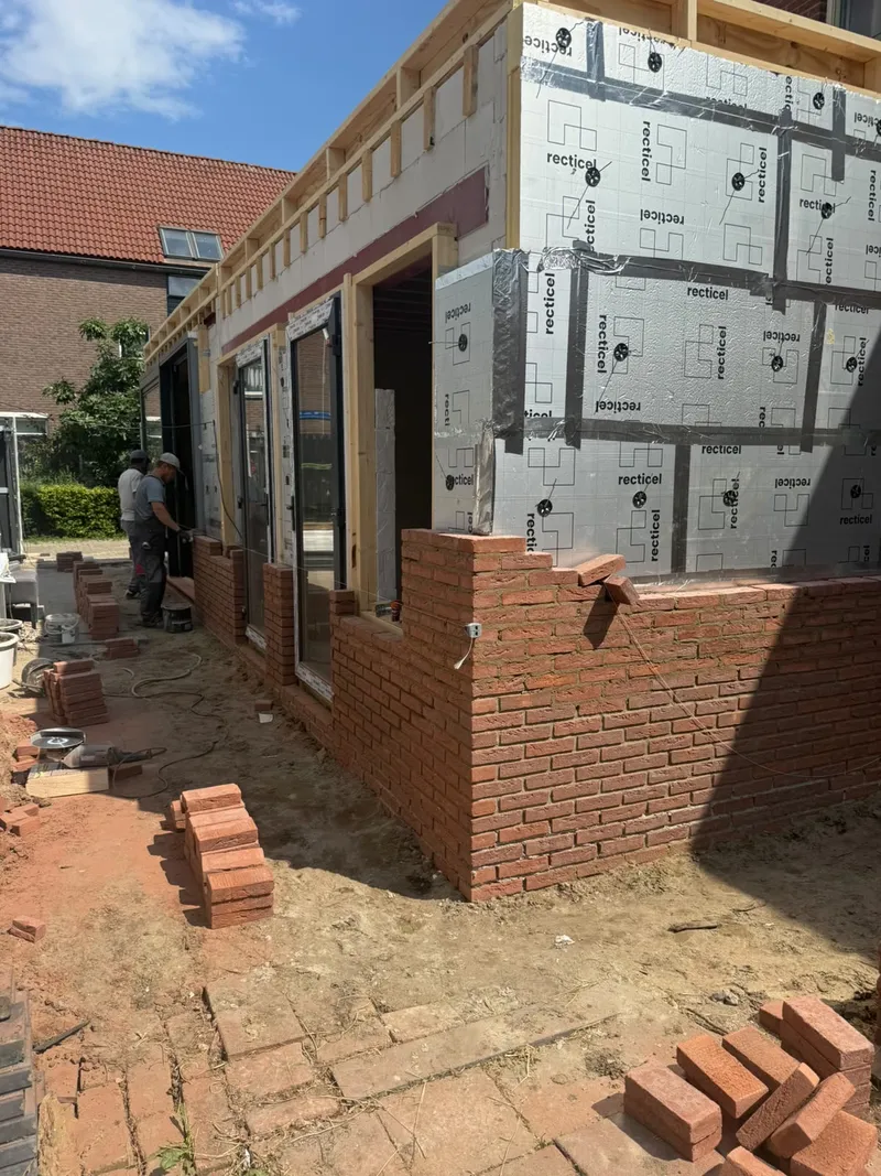 Aanbouw in houtskeletbouw met isolatieplaten op de gevel; het buitenblad in rode baksteen wordt gemetseld