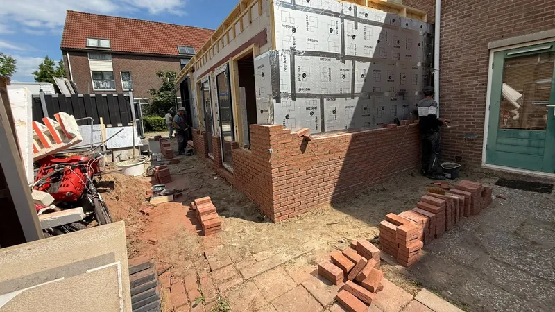 Zijgevel van een aanbouw in houtskeletbouw met isolatieplaten, deels al voorzien van rood metselwerk