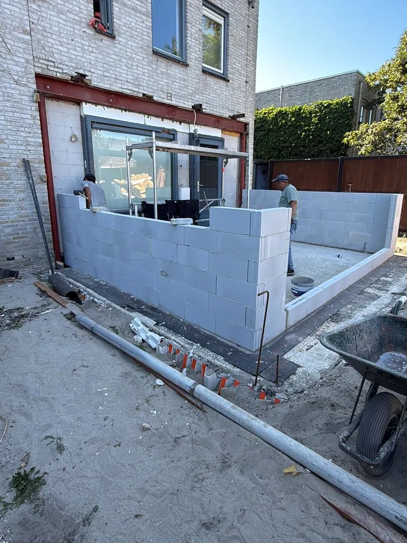 De muren van een aanbouw worden opgetrokken in witte bouwblokken tegen de achtergevel