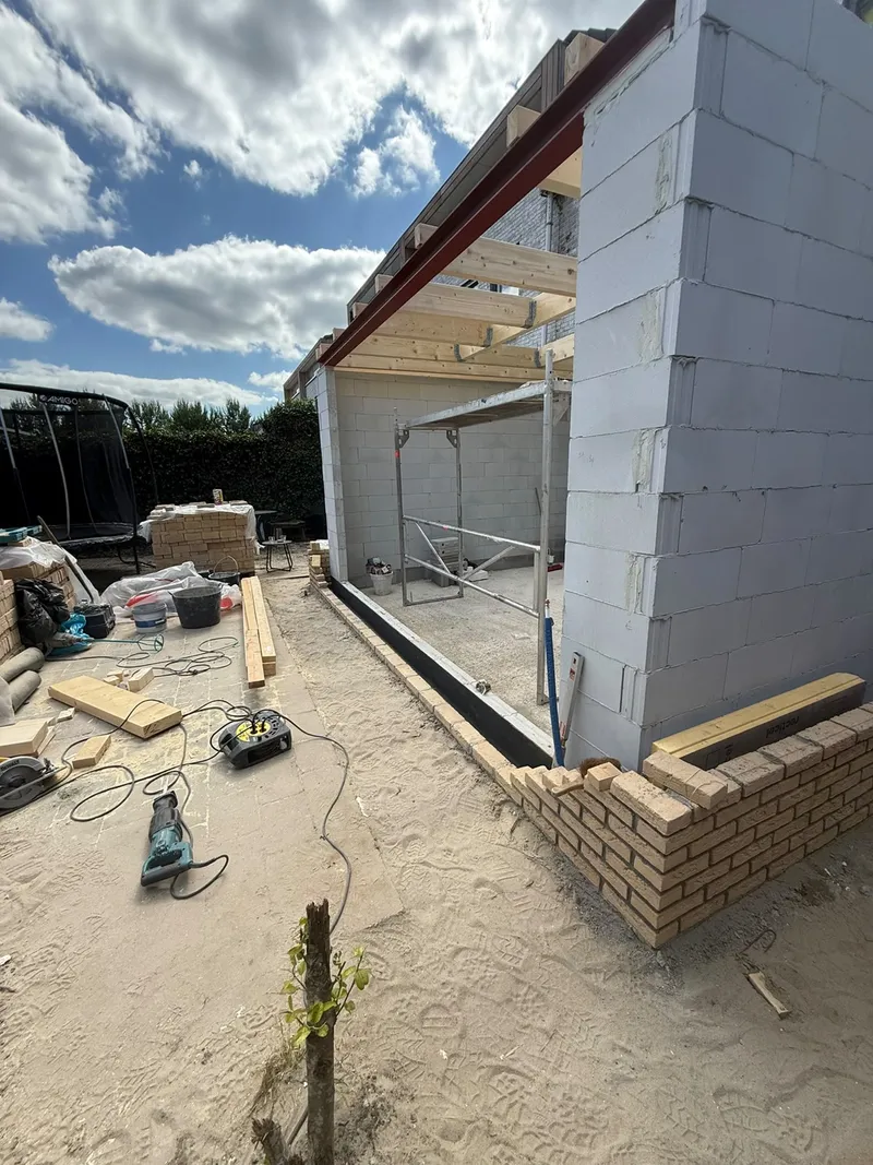 Houten balklaag van het platte dak op de muren van een aanbouw, met het begin van het metselwerk in gele baksteen