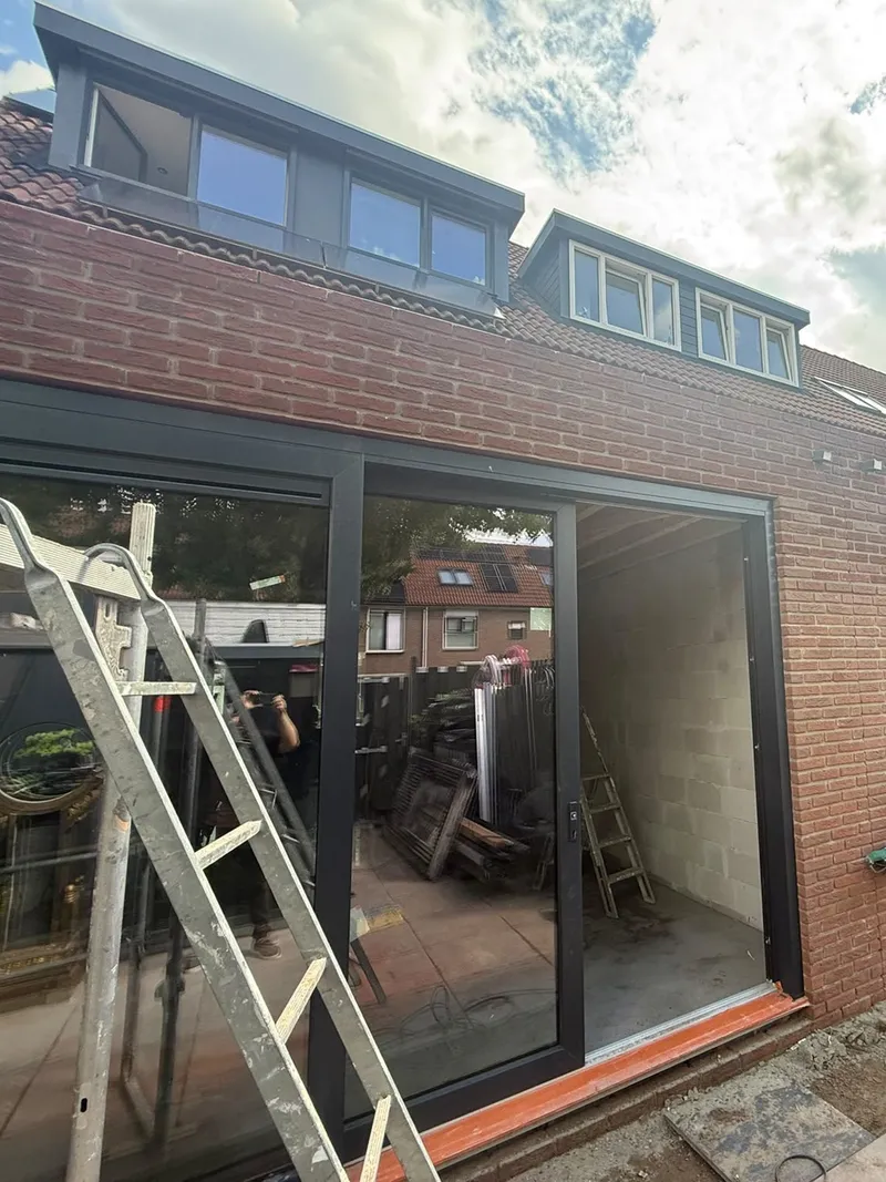 Aanbouw in rode baksteen met een zwarte schuifpui, gezien vanuit de tuin