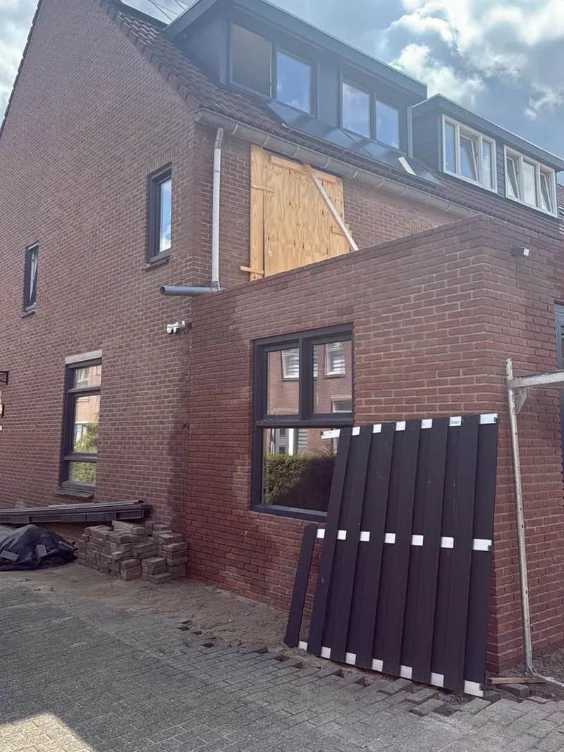 Aanbouw in rode baksteen naast de woning, met een raam in de zijgevel