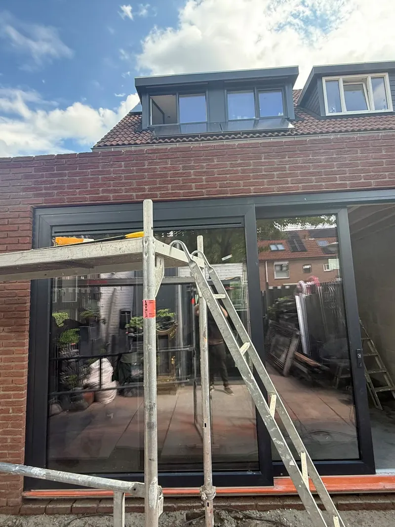 Zwarte schuifpui in de achtergevel van een nieuwe aanbouw in rode baksteen