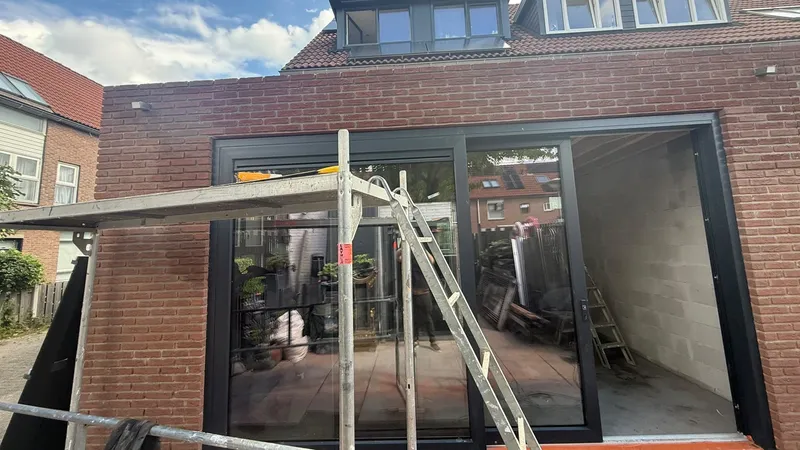 Zwarte schuifpui in de achtergevel van een nieuwe aanbouw in rode baksteen