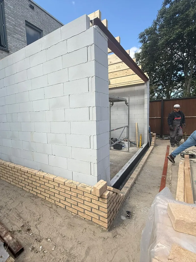 Zijmuur van een aanbouw met een stalen ligger aan de bovenkant en de eerste lagen gele gevelsteen