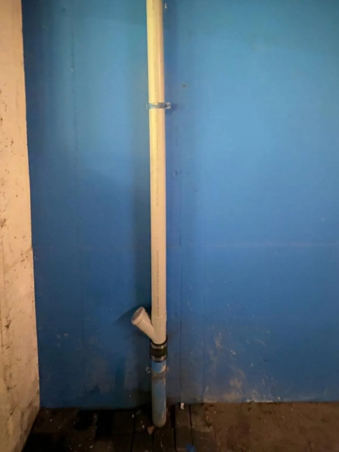 Verticale PVC-afvoerleiding met aftakking langs een wand