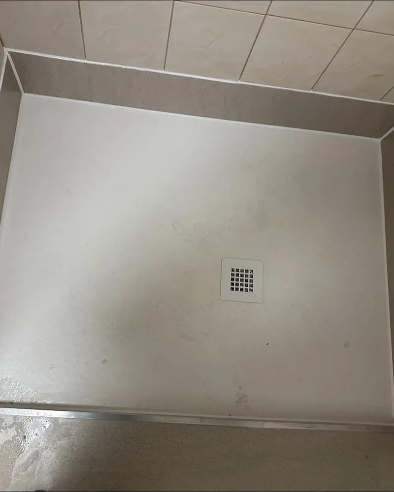 Witte douchebak met vierkant afvoerputje naast een verhoogde vloer met aluminium profiel, van bovenaf