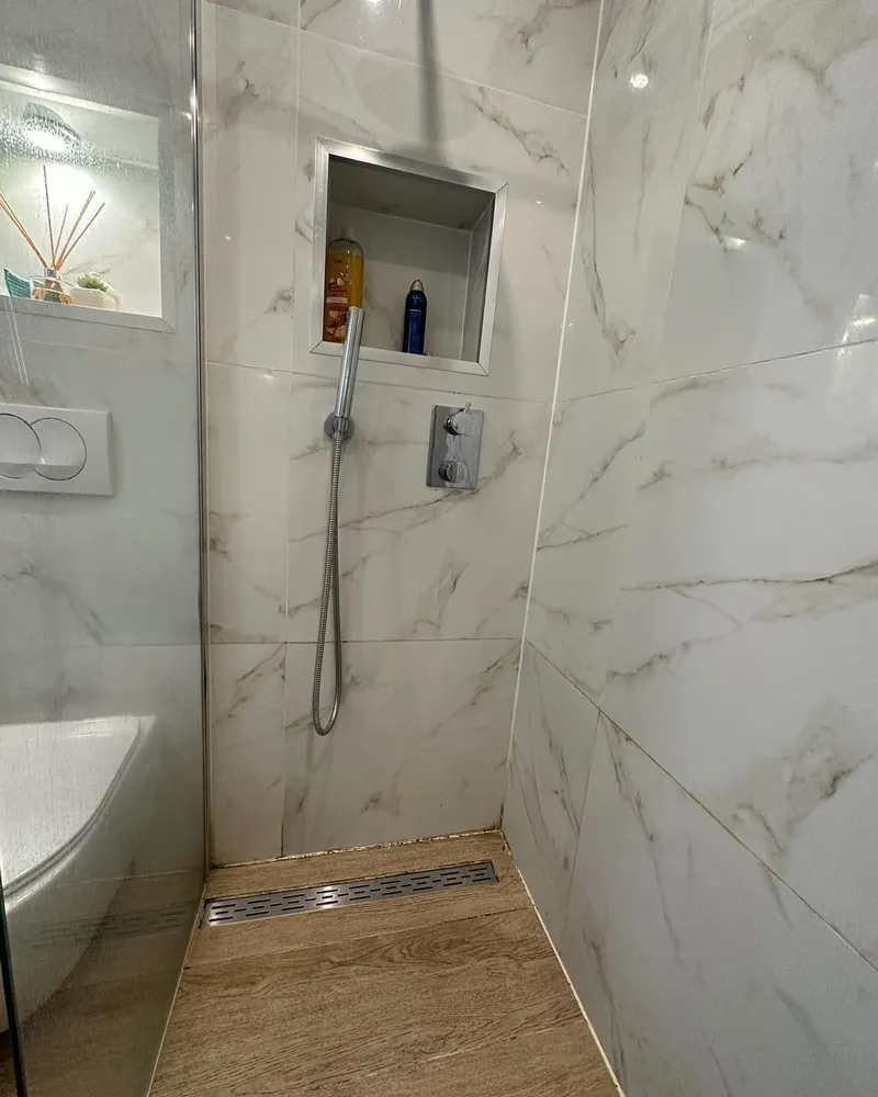 Inloopdouche met handdouche, inbouwkraan, nis en douchegoot in een badkamer met marmerlook tegels en houtlook vloer