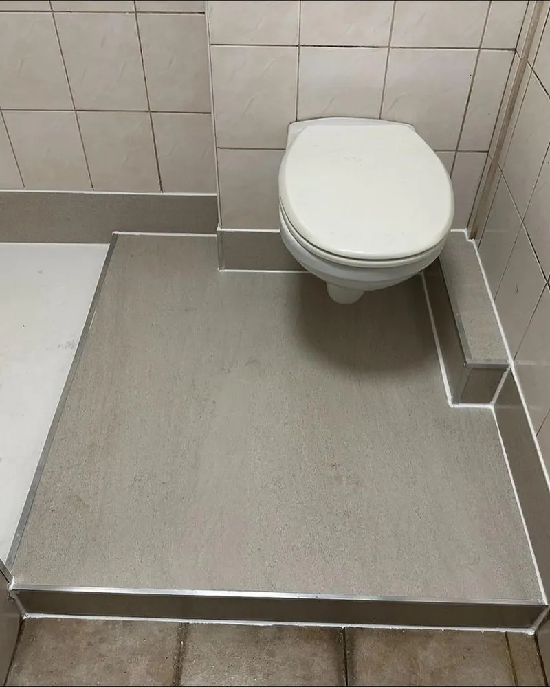 Hangend toilet en witte douchebak op een verhoogde vloer met grijze afwerking en aluminium hoekprofielen