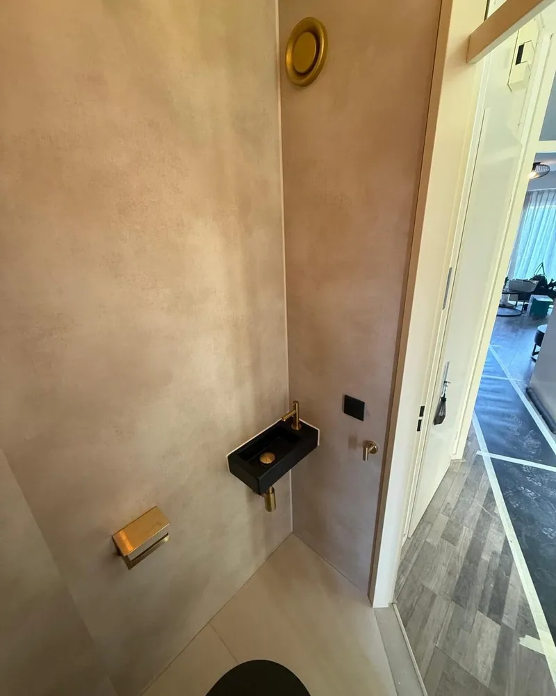Zwarte fontein met goudkleurige kraan, goudkleurige toiletrolhouder en ventilatierooster in de gerenoveerde toiletruimte