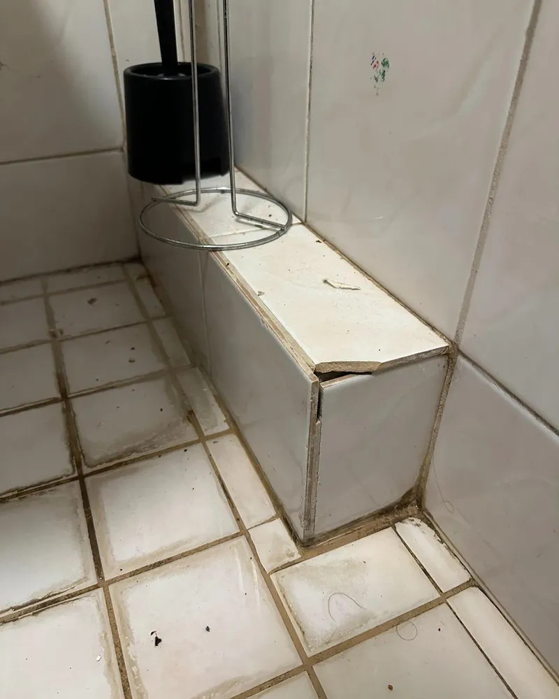 Betegelde toiletombouw met een afgebroken hoektegel en vervuilde voegen