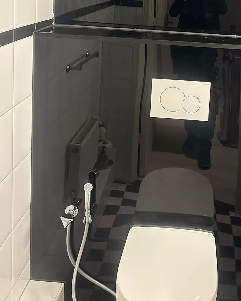 Hangend toilet met bedieningsplaat en bidetsproeier in een toiletruimte met zwart-witte vloertegels