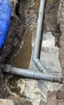Grijze PVC-rioolbuizen met bocht en aansluiting in een uitgegraven sleuf