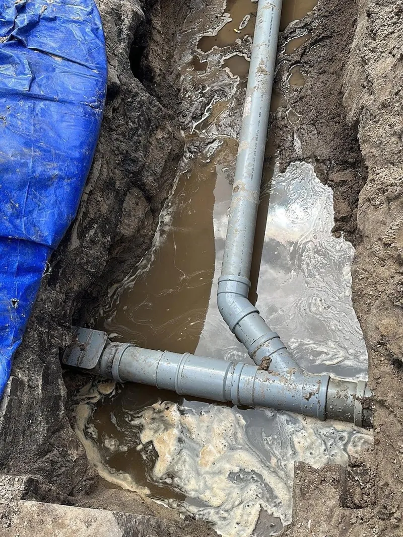 Grijze PVC-rioolbuizen met bocht en aansluiting in een uitgegraven sleuf