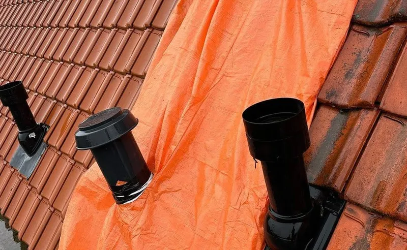 Drie zwarte ontluchtingspijpen op oranje dakfolie tussen de rode dakpannen
