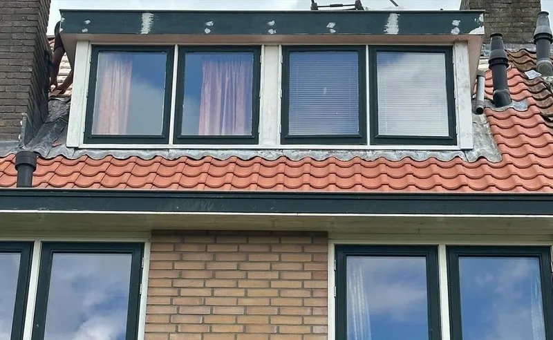 Dakkapel met ramen op een pannendak met rode dakpannen, boven een bakstenen gevel