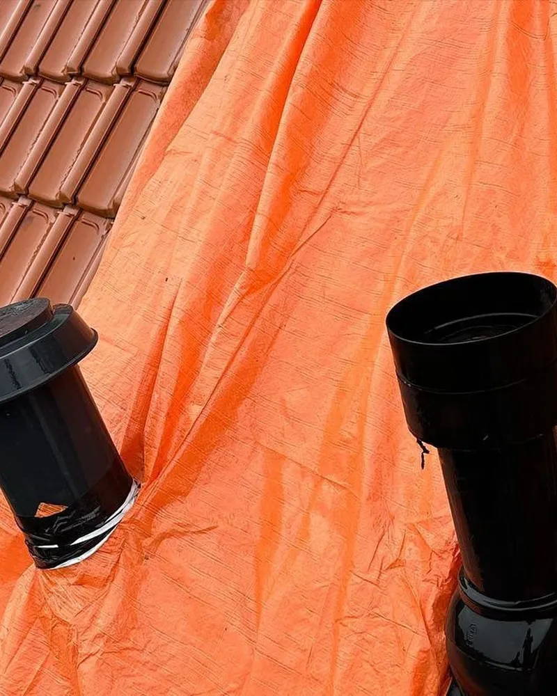 Zwarte ontluchtingspijpen op oranje dakfolie tussen de rode dakpannen