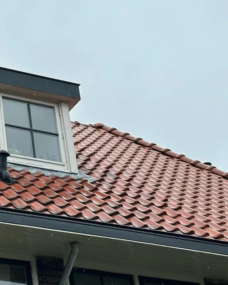 Hellend dak met rode keramische dakpannen, een dakkapel en een dakgoot met regenpijp