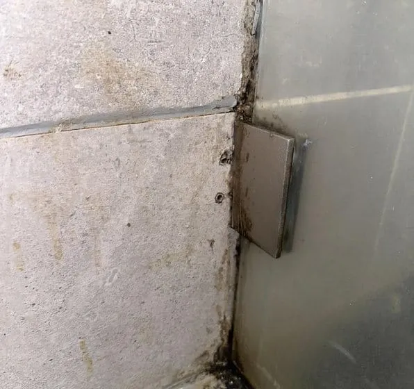Zwarte schimmel en vervuiling in de kitrand van een douchehoek naast de glazen wand