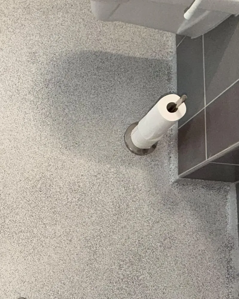 Afgewerkte epoxy vlokkenvloer in een toiletruimte met toiletrolhouder
