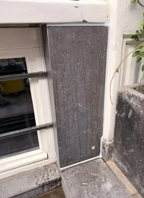 Tweede gevelvlak naast het souterrainraam, afgewerkt met een donkergrijze natuurstenen plaat en een witte kitvoeg
