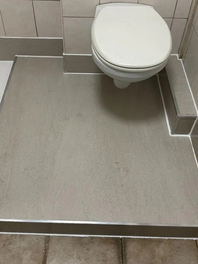 Hangend toilet op een verhoogde vloer met strakke grijze afwerking en aluminium hoekprofielen
