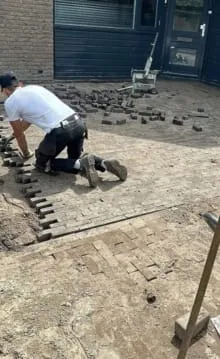 Klinkers worden opnieuw gelegd voor een woning, met een stenenknipper op de achtergrond
