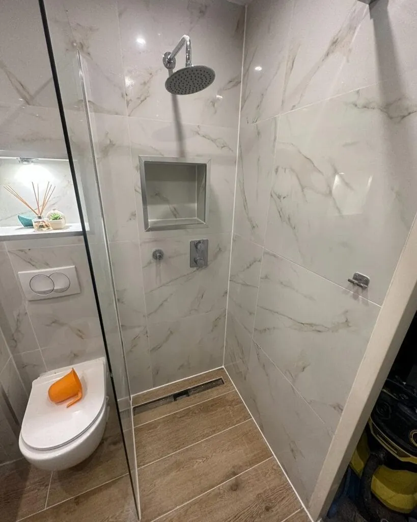 Kleine badkamer met inloopdouche, marmerlook tegels, inbouwkraan, douchegoot en hangend toilet