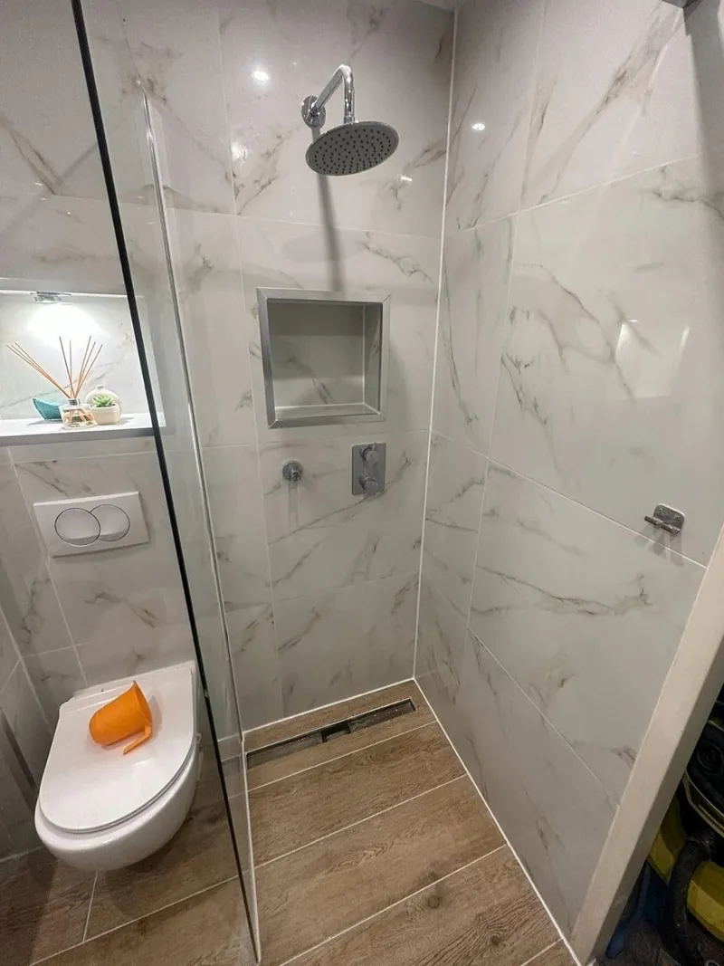 Kleine badkamer met inloopdouche, marmerlook tegels, inbouwkraan, douchegoot en hangend toilet