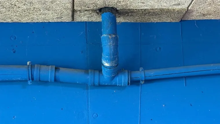 Met tape omwikkelde aansluiting van een afvoerleiding tegen een blauw geschilderde wand