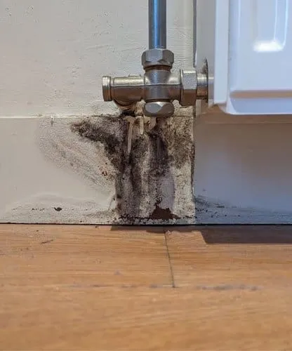 Schimmel en vochtschade rond een radiatoraansluiting vóór reparatie