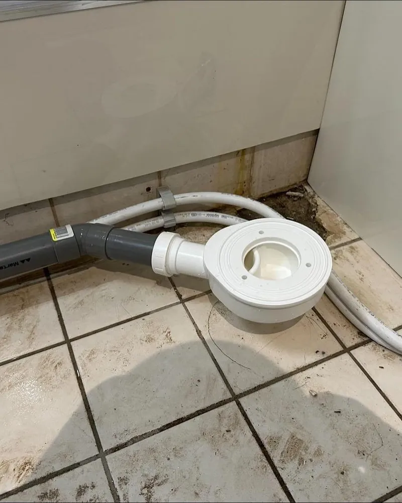 Witte douchesifon met grijze PVC-afvoer en waterslang op een tegelvloer tijdens de verbouwing