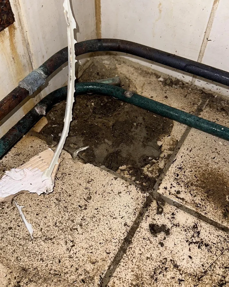 Oude gecorrodeerde leidingen langs de vloer van een gestripte badkamer