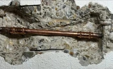 Nieuw stuk koperen waterleiding met koppelingen in de opengehakte wand, na het verhelpen van de lekkage