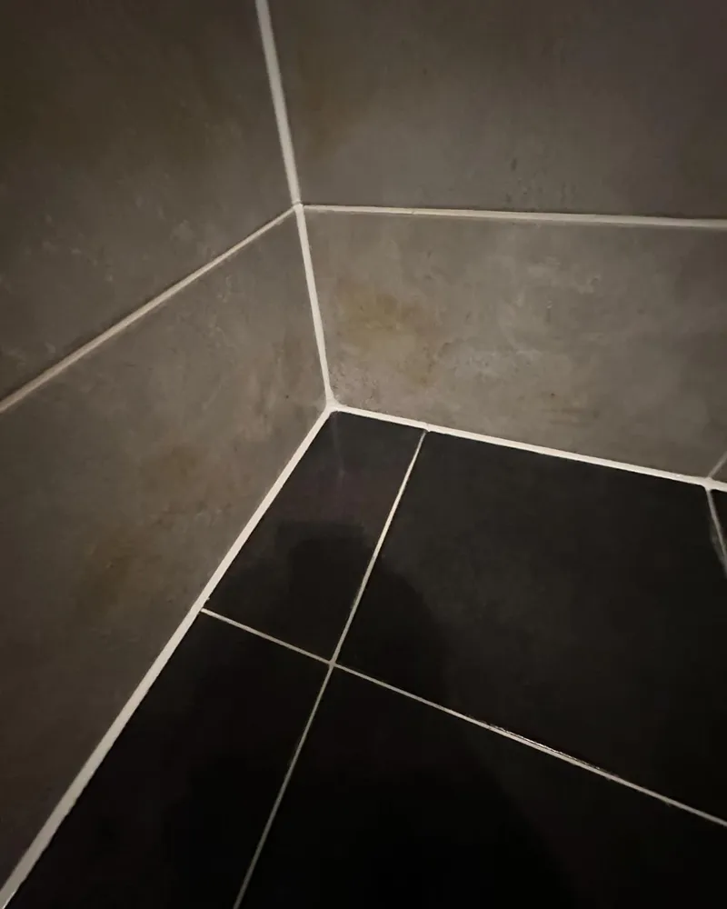 Nieuwe witte kitranden in de hoek van een douche met grijze wandtegels en zwarte vloertegels