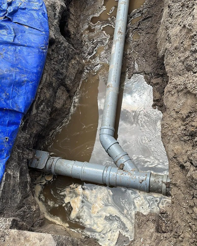 Grijze PVC-rioolbuizen met bocht en aansluiting in een uitgegraven sleuf
