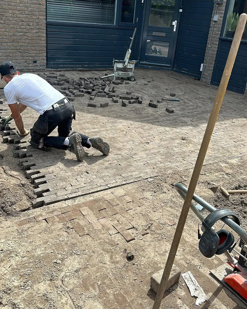 Klinkers worden opnieuw gelegd voor een woning, met een stenenknipper op de achtergrond