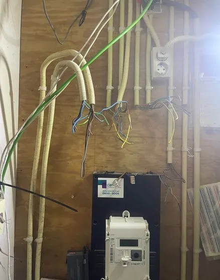Meterkast met houten achterwand nadat de oude kast is verwijderd; de bedrading hangt klaar
