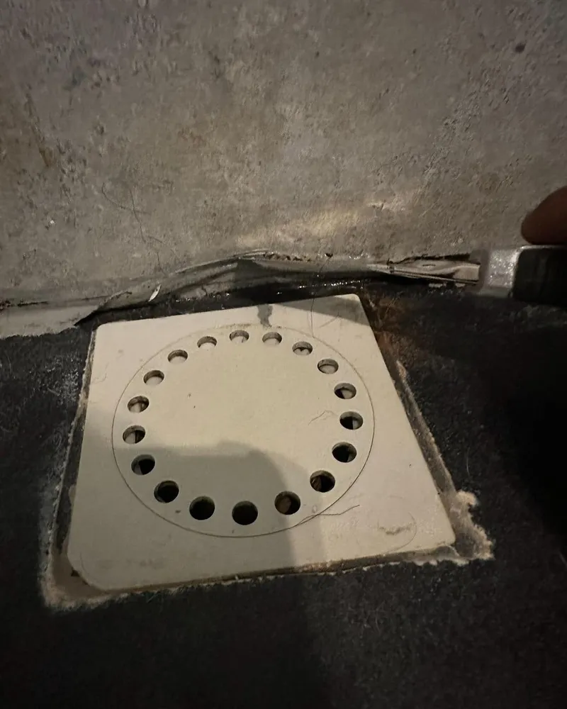 Nieuwe vierkante vloerput met rond rooster, ingewerkt in een zwarte waterdichte laag tegen een betonwand