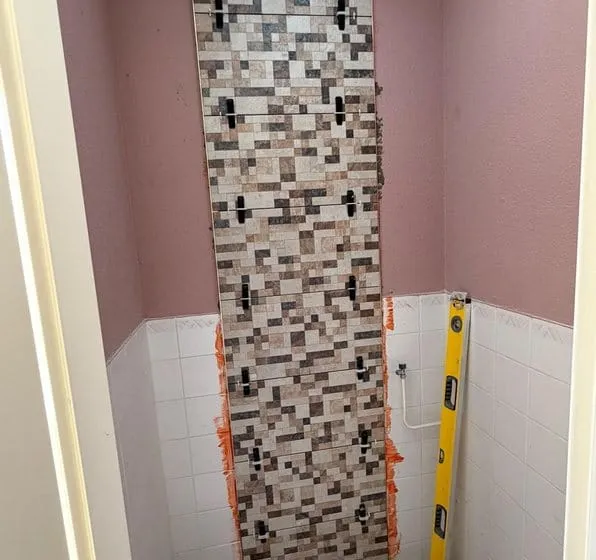Toiletruimte tijdens het tegelen: een verticale strook mozaiektegels met tegelclips tegen de achterwand
