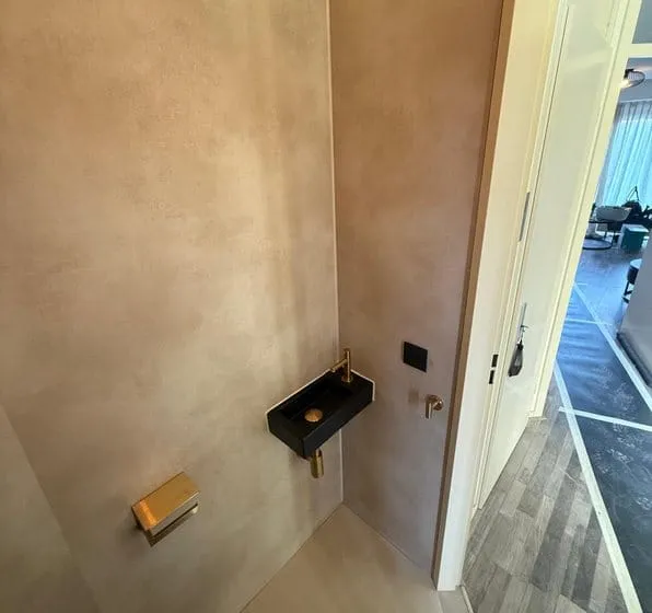 Zwarte fontein met goudkleurige kraan, goudkleurige toiletrolhouder en ventilatierooster in de gerenoveerde toiletruimte