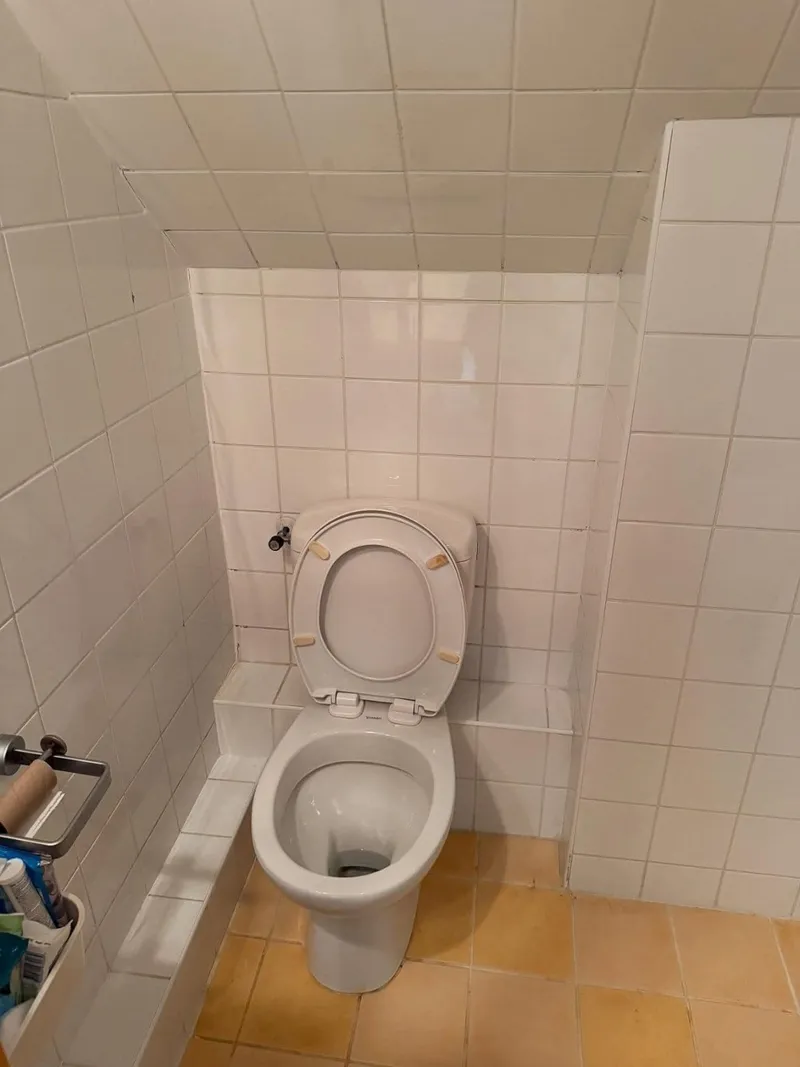 Staand toilet onder een schuin plafond, vóór de renovatie naar een hangend toilet
