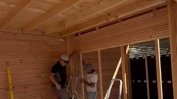 Twee vakmensen bevestigen de houten wandbekleding aan de achterwand van een overkapping