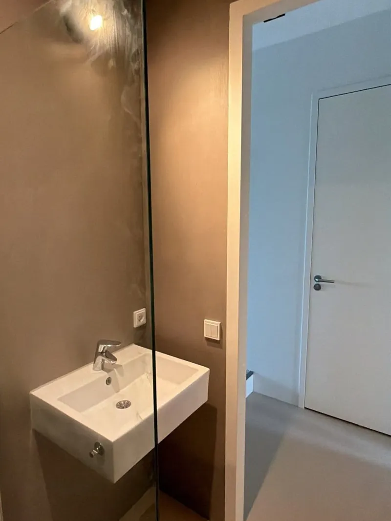 Zwevende wastafel met kraan naast een glazen douchewand